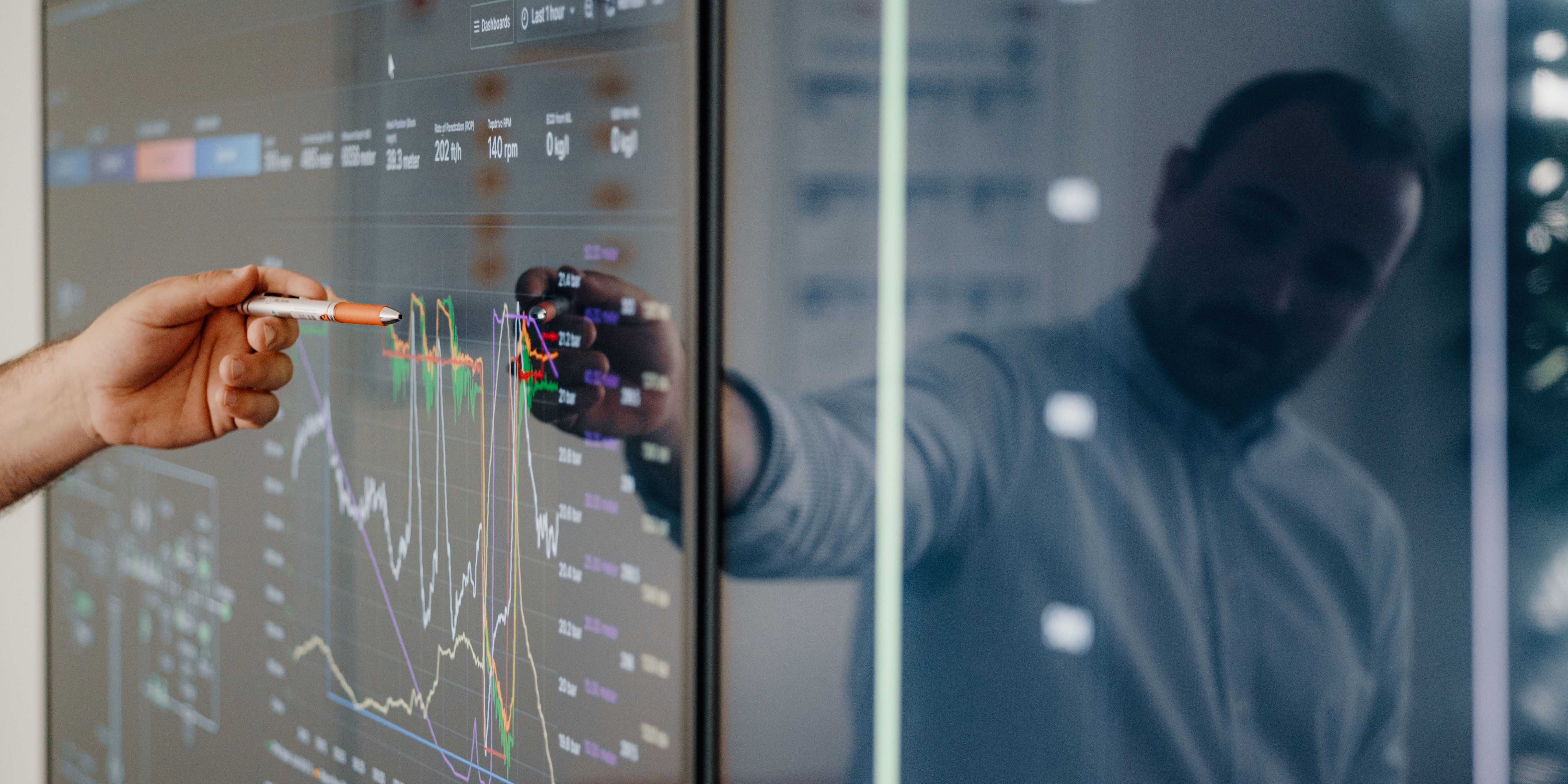 Man pointing at graphs on screen with pen