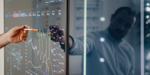 Man pointing at screen showing graphs with pen