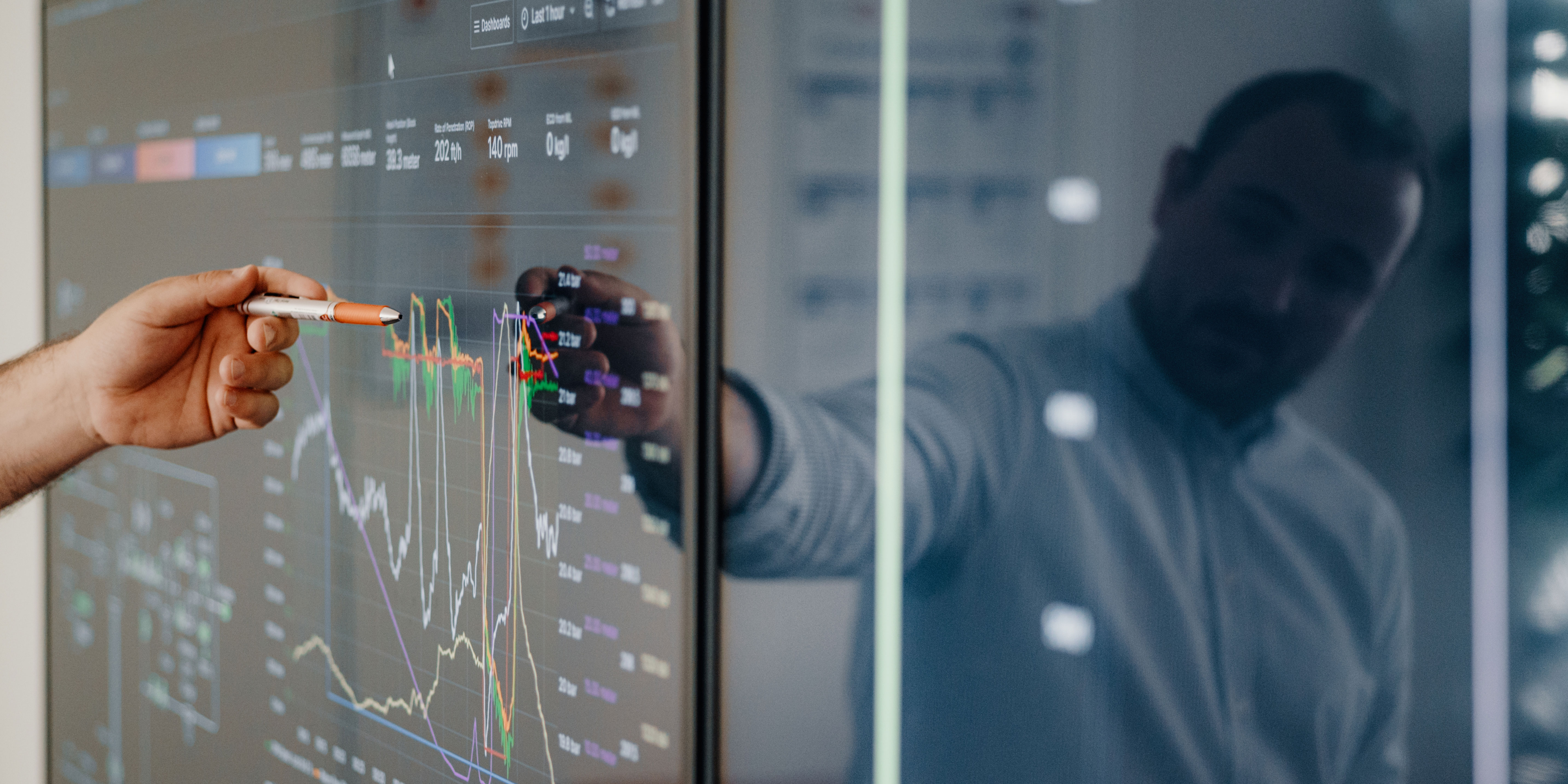 Man pointing at screen showing graphs with pen